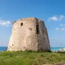 La torre di Torre Mozza sul prato, con il mare turchese alle spalle