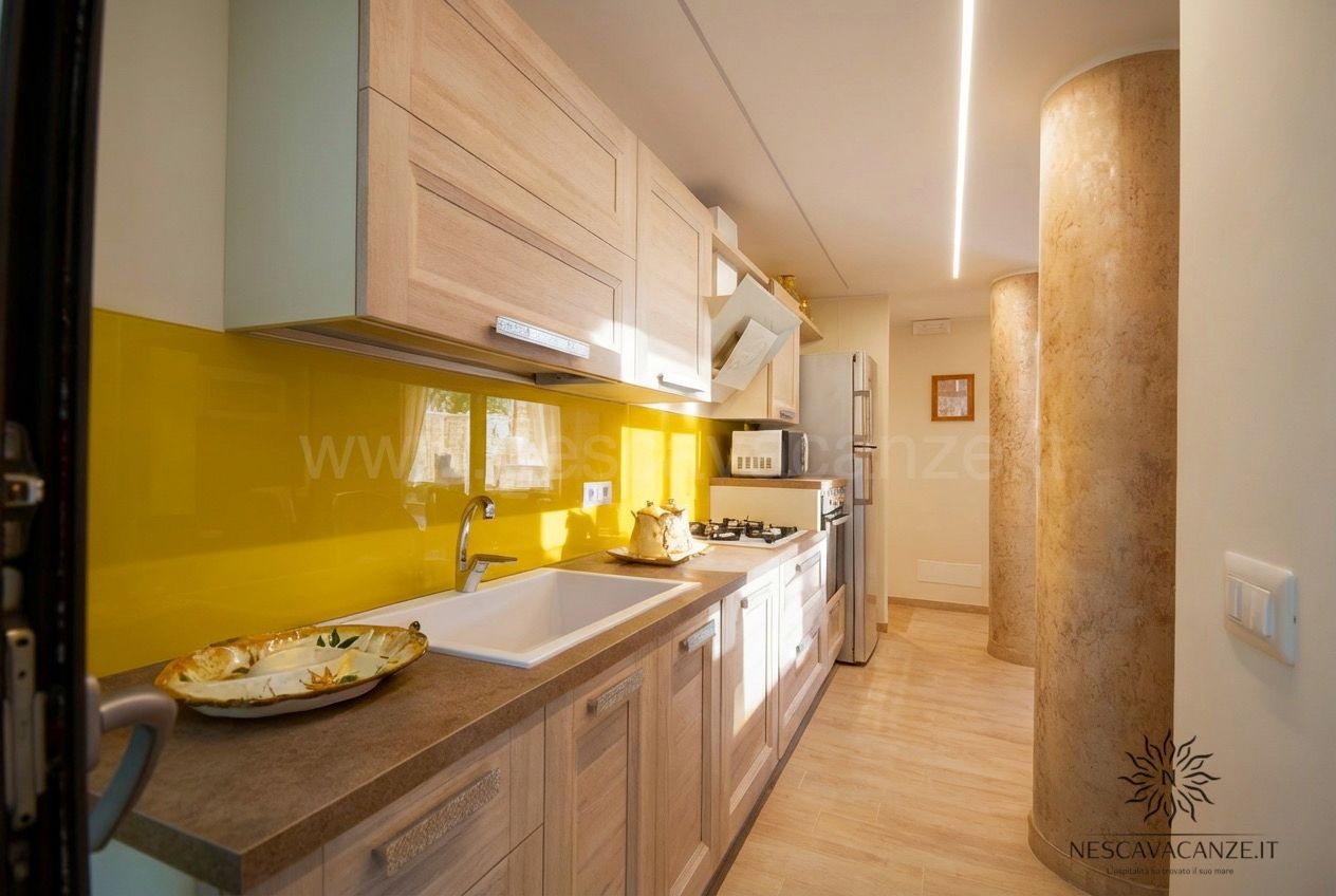 Casa Salento - cucina lineare in legno chiaro con paraschizzi giallo, lavello e colonna decorativa