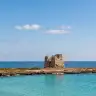 Acqua turchese e fondale chiaro con la Torre Zozzoli sulla punta