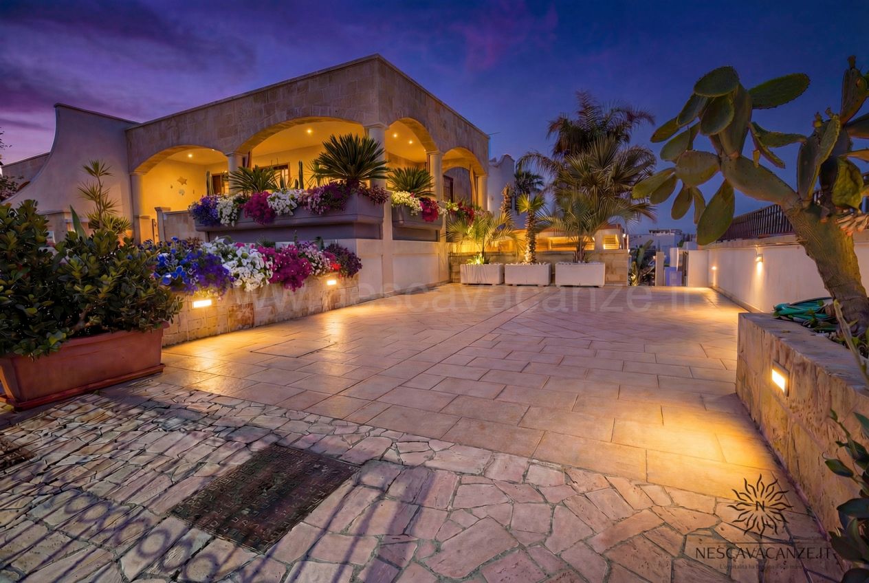 Casa Pescoluse 2 - cortile fiorito illuminato al tramonto con loggiato ad archi e cactus