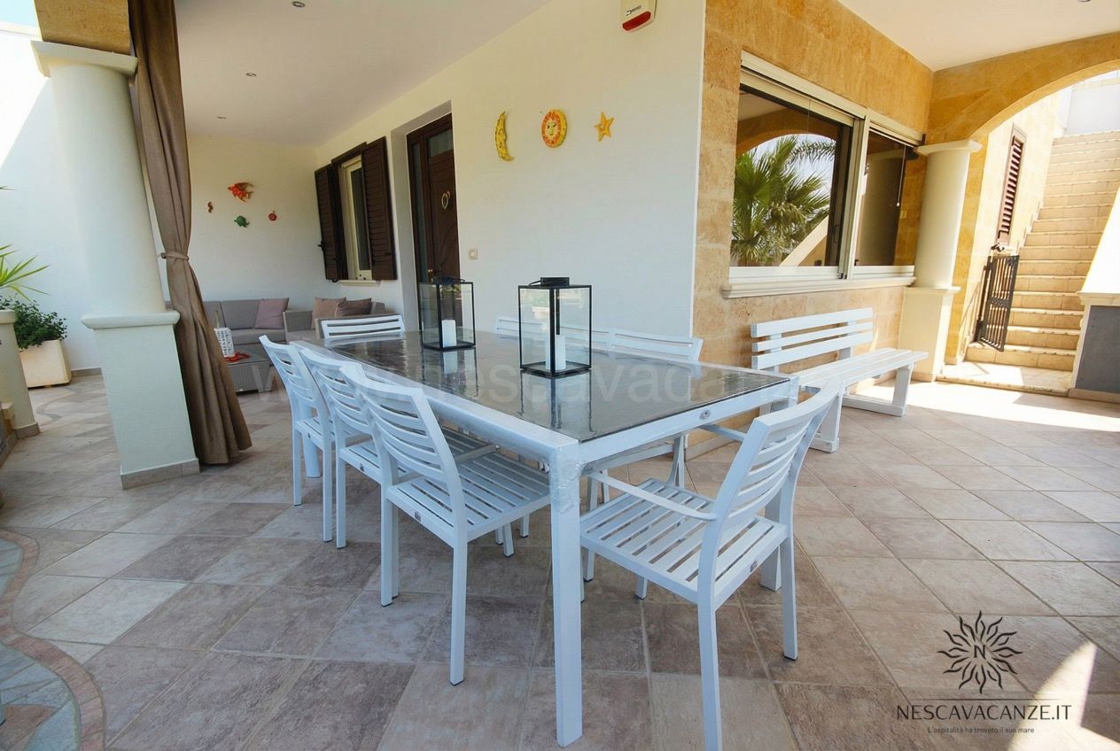 Casa Pescoluse 1 - veranda coperta con tavolo, sedie e panca bianche, lanterne e vista giardino