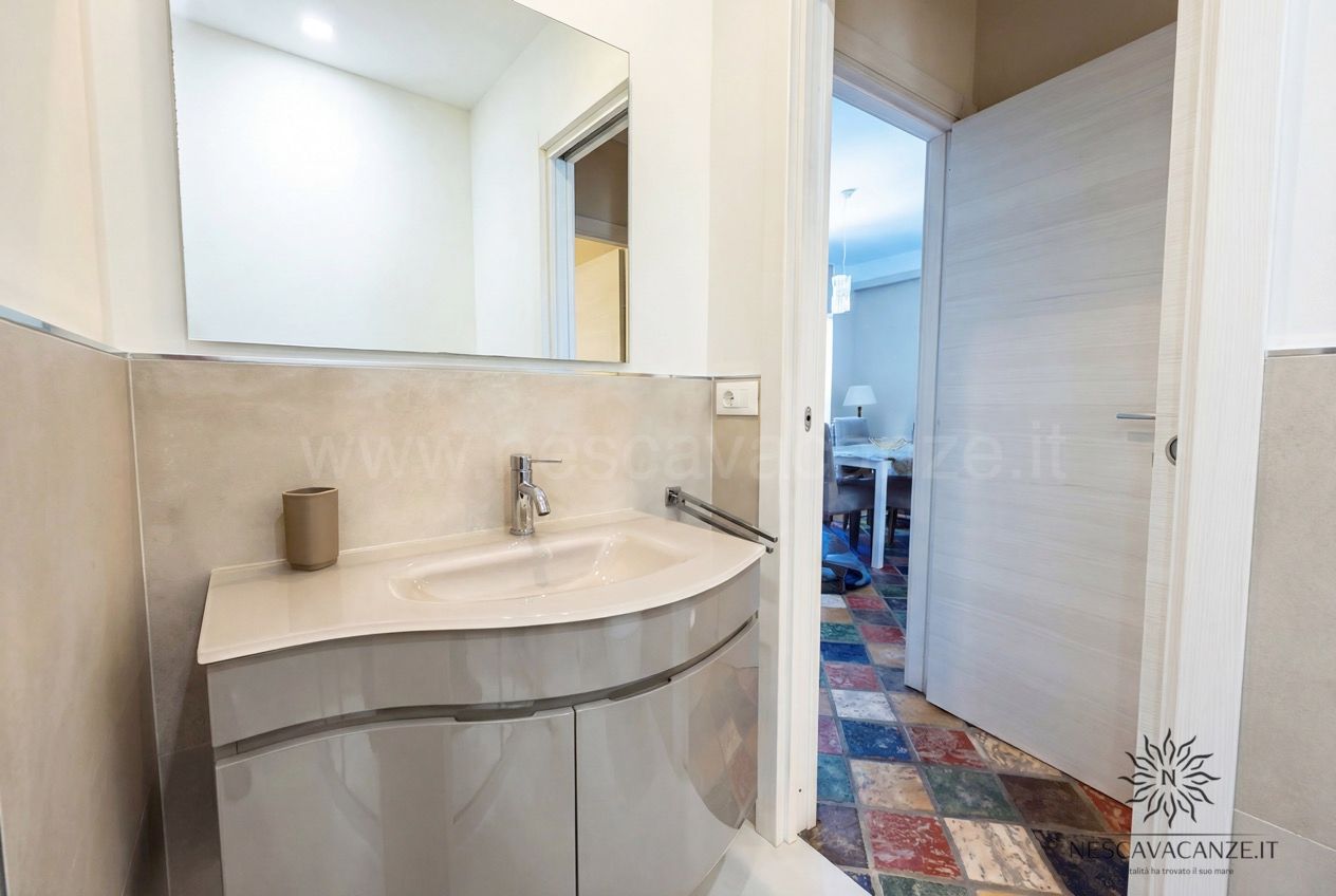 Casa Sabbia Oro - bagno con lavabo curvo, ampio specchio e vista sulla zona pranzo