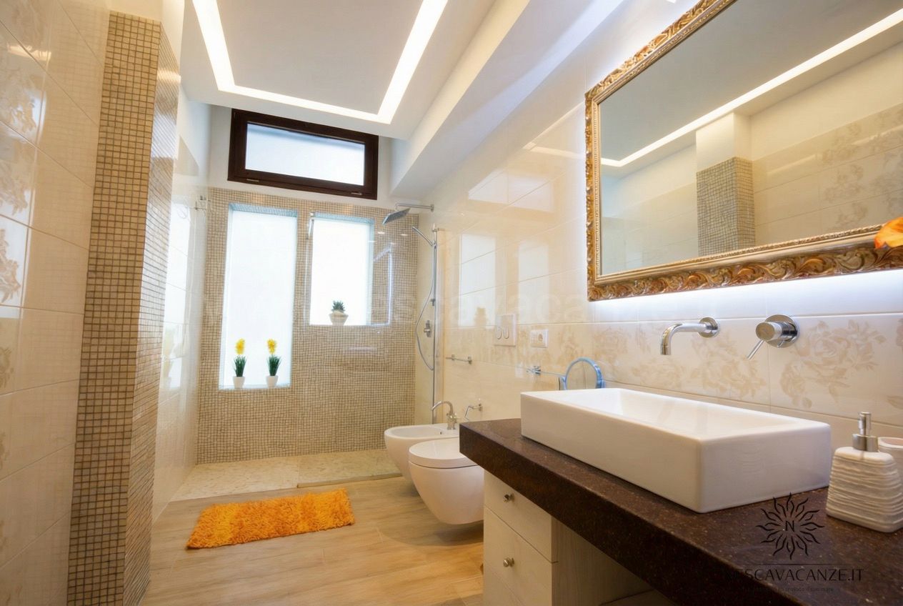 Casa Salento - bagno beige con doccia a mosaico, doppio lavabo, specchio dorato, wc e bidet