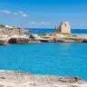 La torre di Roca Vecchia sugli scogli, con il mare blu e trasparente