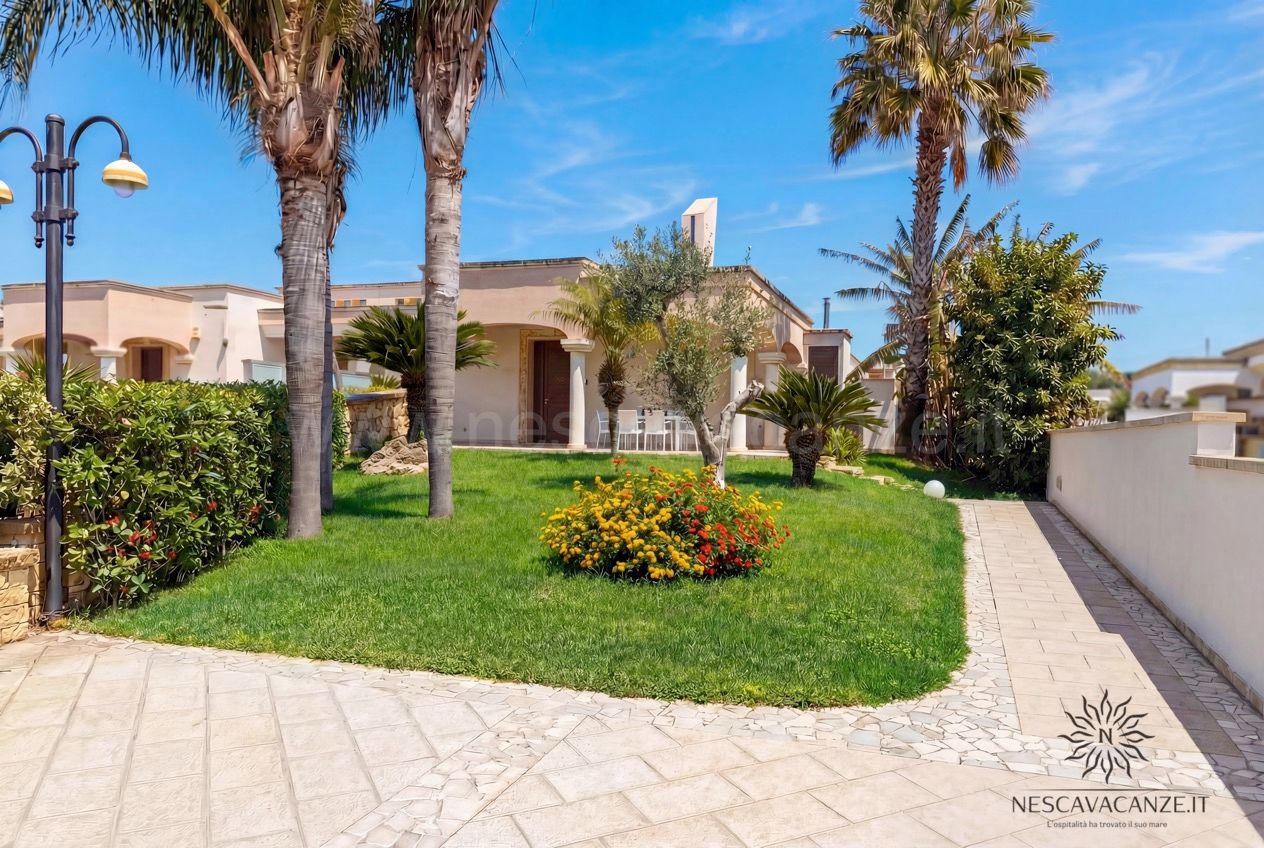 Casa Pescoluse 8 - Giardino curato con prato, palme, ulivo e aiuola fiorita davanti alla villa
