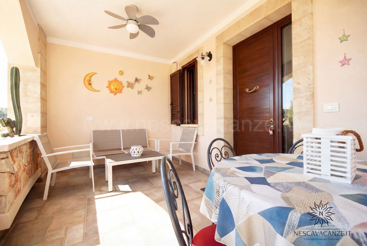 Casa Pescoluse 4 - veranda con divanetto, poltrone, tavolo, porta in legno e decori sole e luna