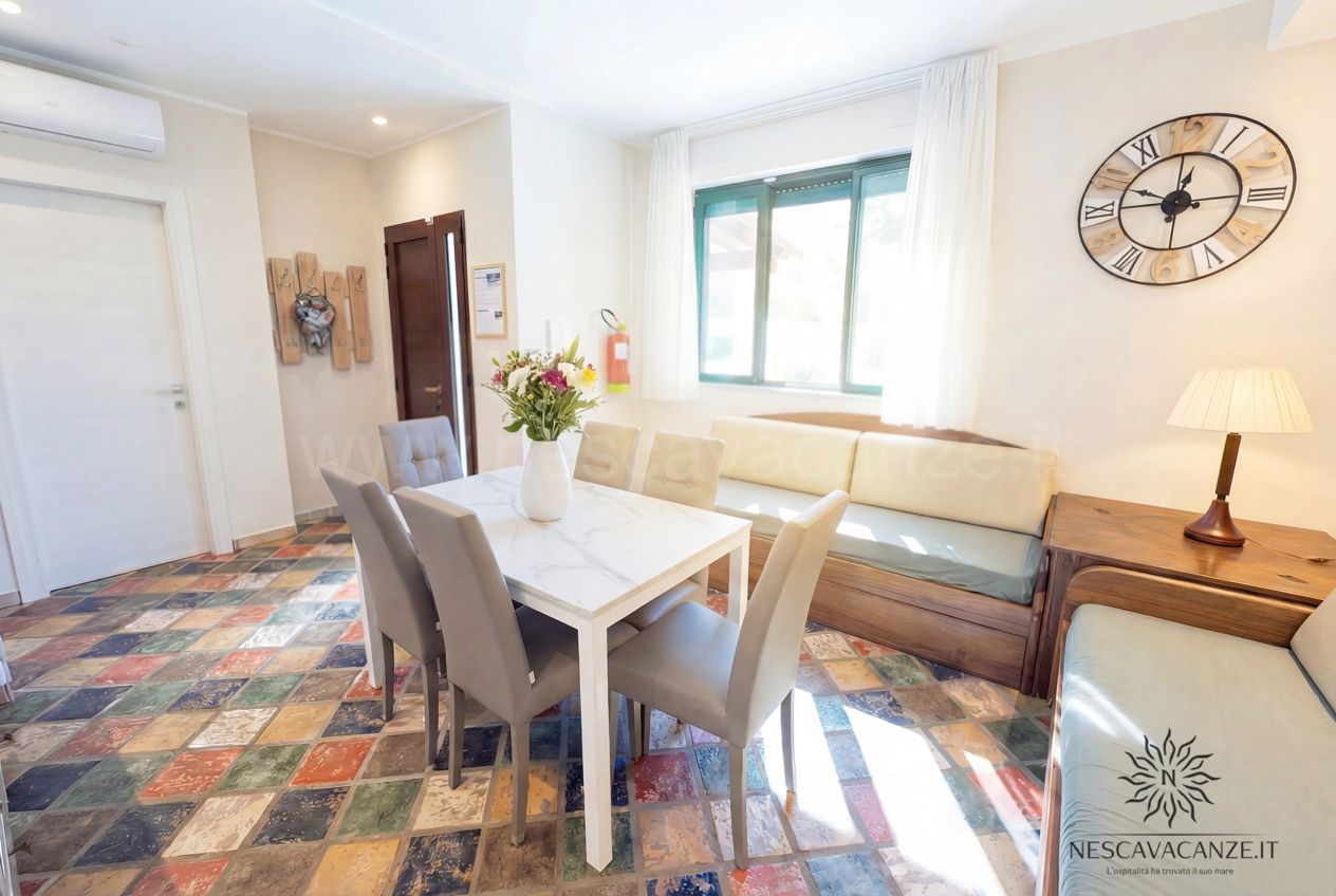 Casa Sabbia Oro - soggiorno con tavolo, due divani in legno, orologio a parete e lampada