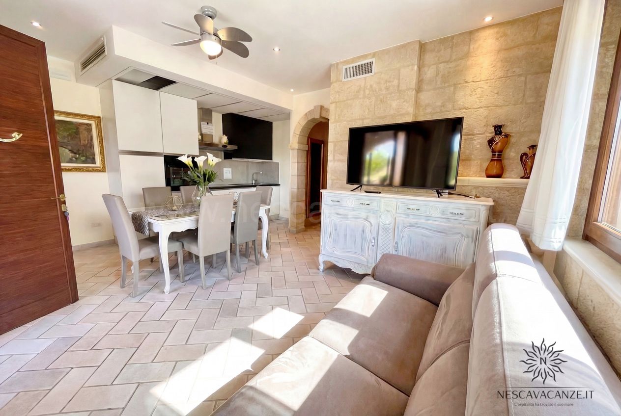 Casa Pescoluse 4 - soggiorno con divano, TV su credenza anticata, angolo cottura e tavolo da pranzo