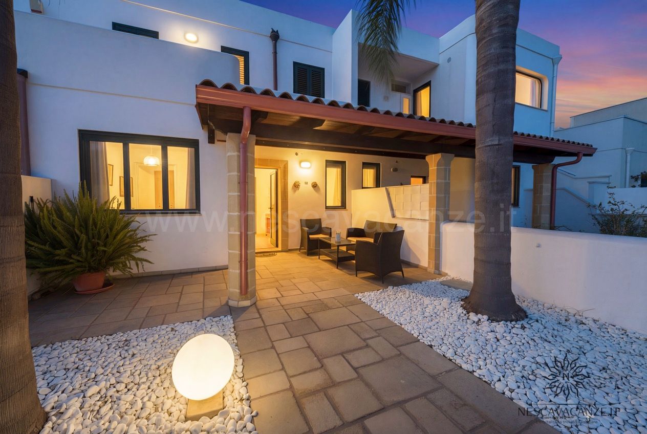 Casa Sabbia Oro - veranda illuminata al crepuscolo con poltroncine, lampada sferica e ciottoli bianchi