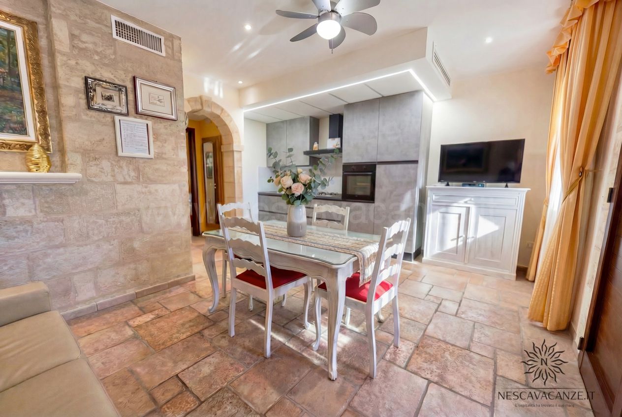 Casa Pescoluse 5 - soggiorno con tavolo da pranzo, cucina, TV, divano e parete in pietra