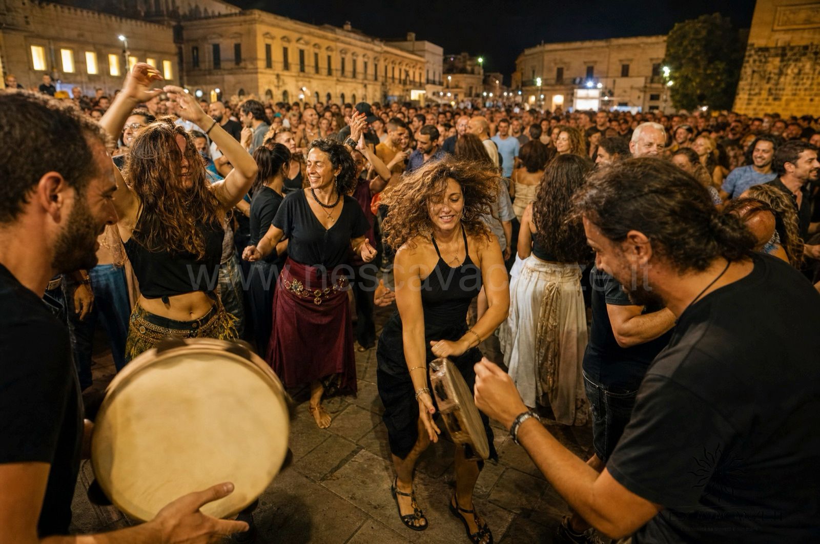 Folla che balla la pizzica di notte in piazza durante una serata di musica popolare salentina
