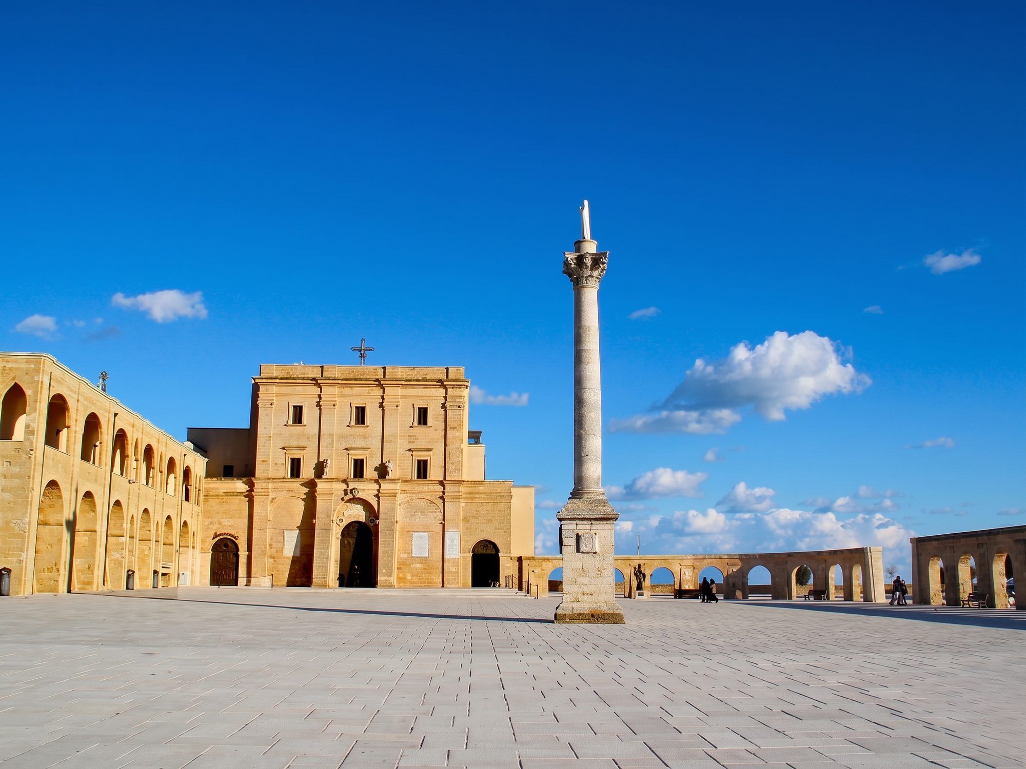 La facciata in pietra chiara della basilica de Finibus Terrae, con la colonna sul piazzale