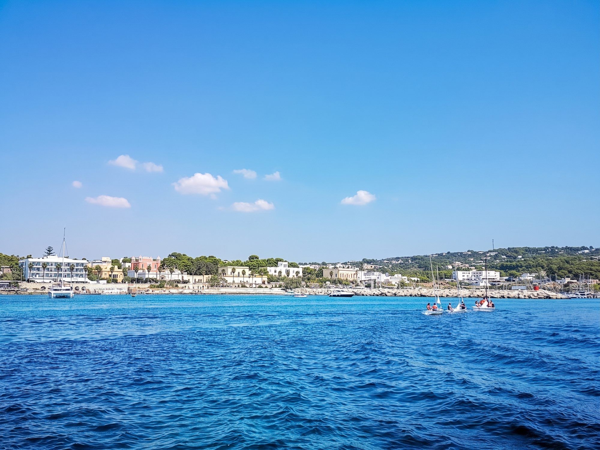 Il lungomare di Santa Maria di Leuca visto dal mare blu, con le ville e i pini