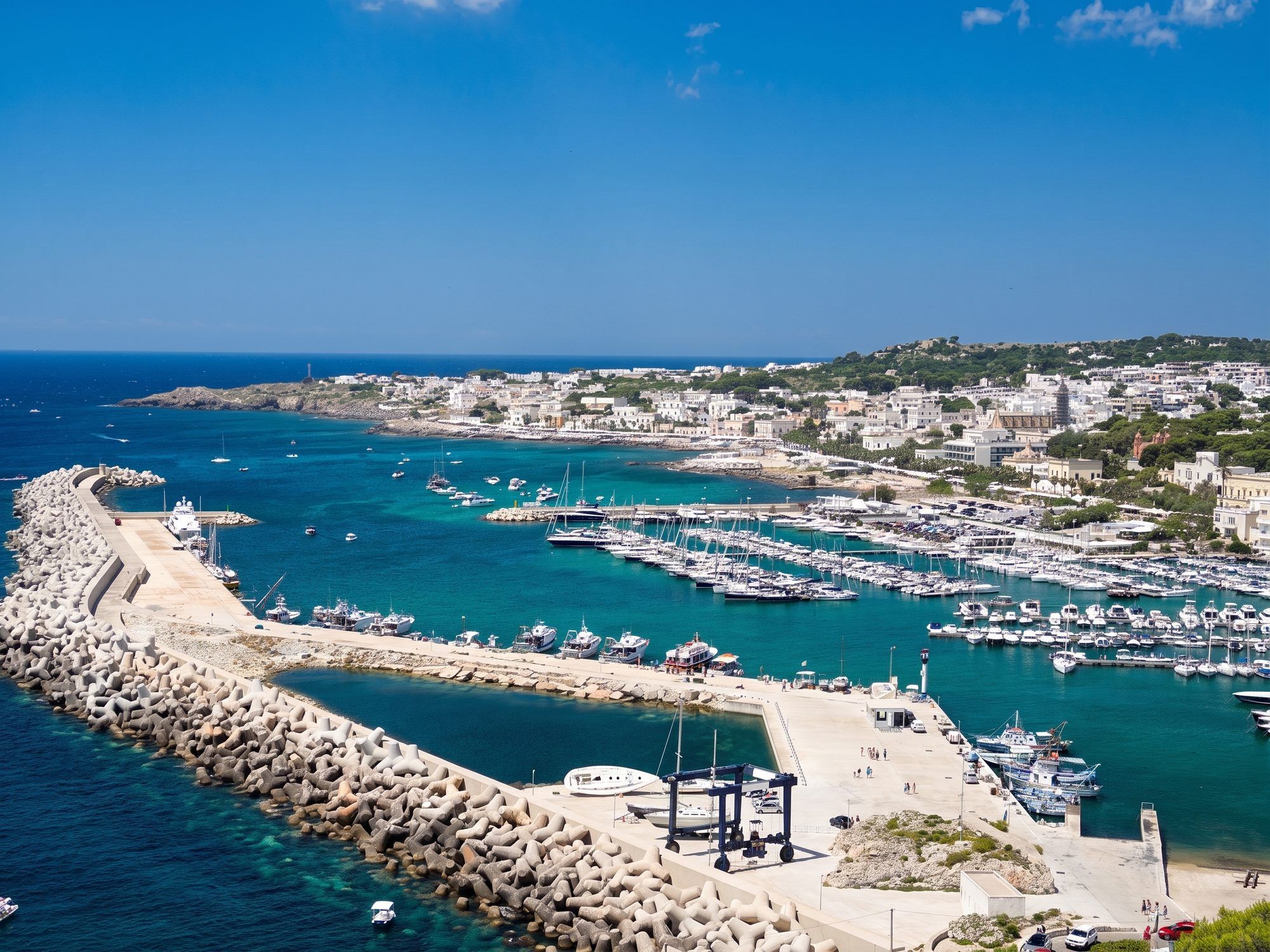 Il porto turistico di Leuca con la diga di massi, le barche e il paese bianco sulla costa