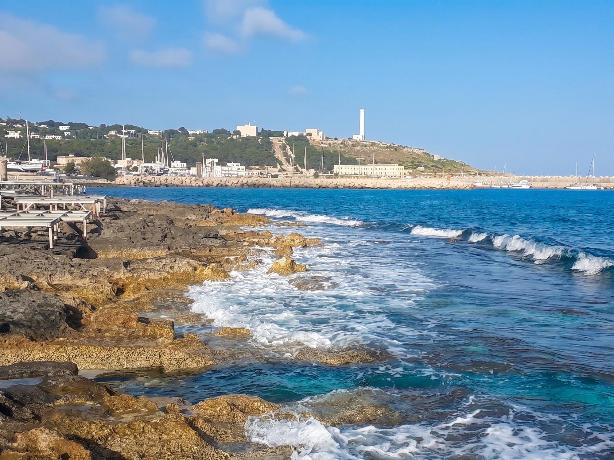 Scogli piatti battuti dalle onde sul lungomare di Leuca, con il faro in lontananza sul capo