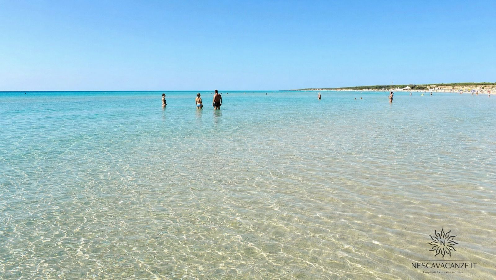 I fondali bassi e trasparenti di Pescoluse con persone che camminano nell'acqua turchese lontano dalla riva, sopra la sabbia chiara