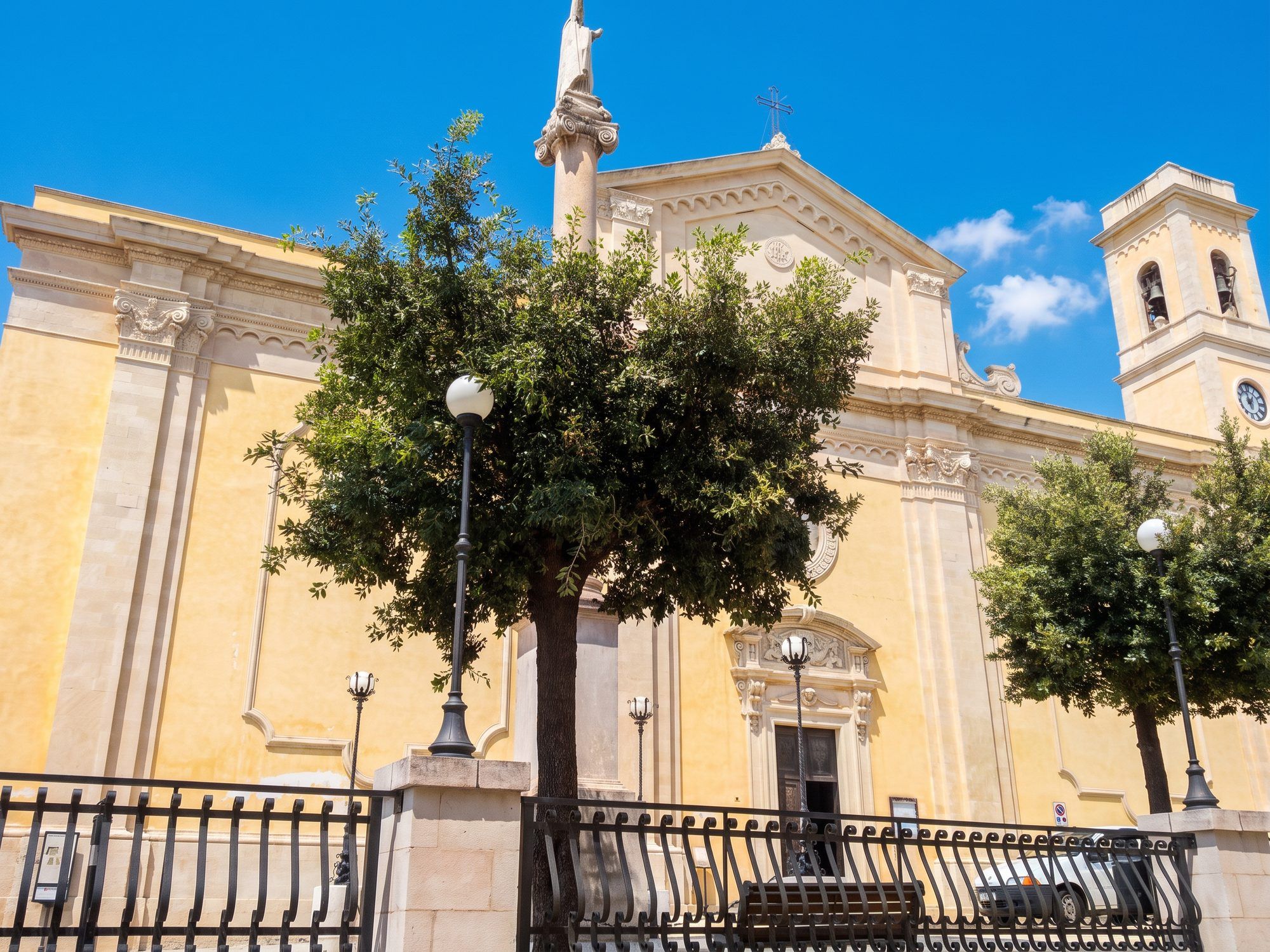 La facciata chiara della chiesa madre di San Nicola Magno a Salve, con il campanile e gli alberi davanti
