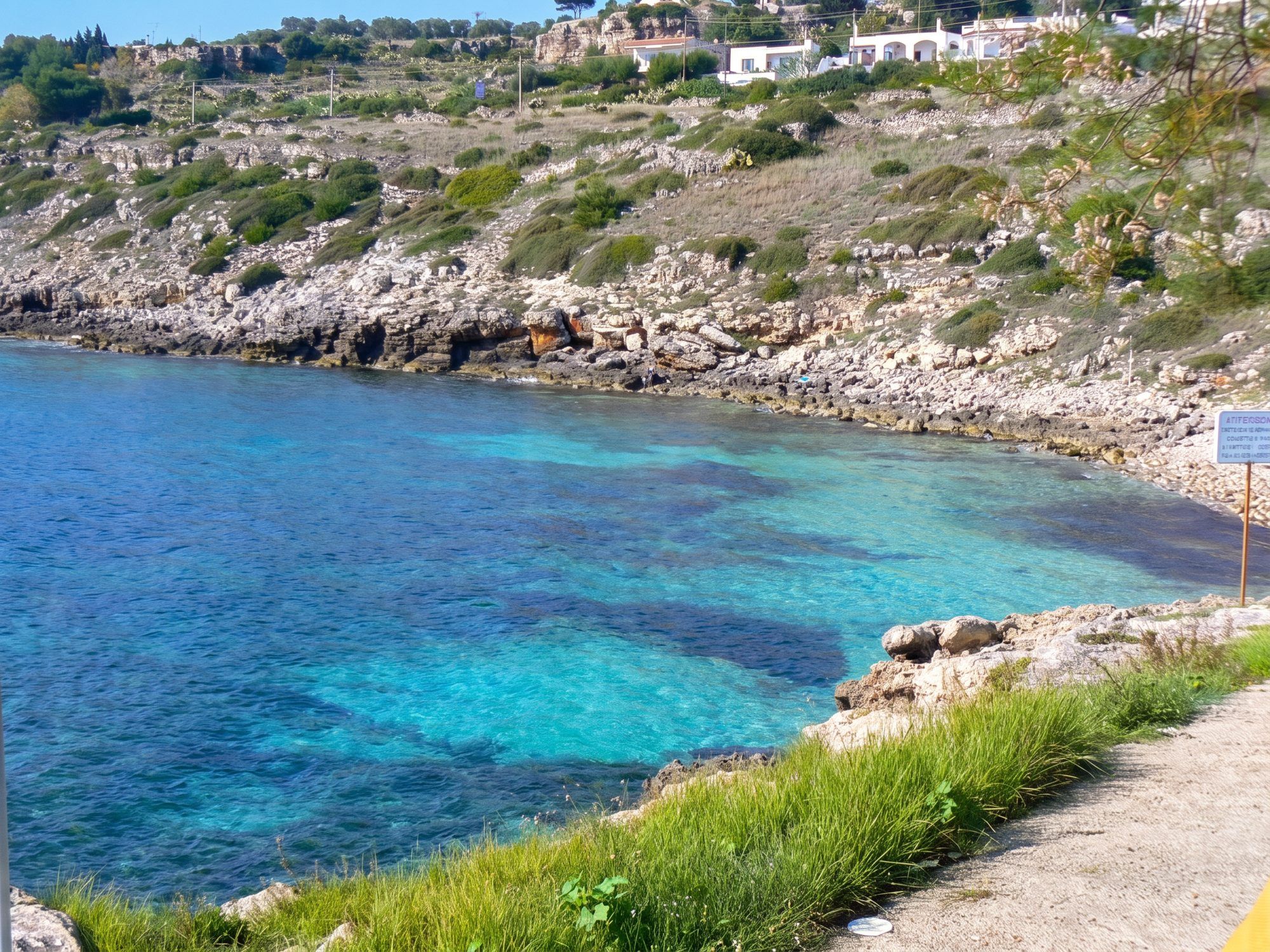 La baia di San Gregorio con l'acqua turchese sotto la costa di roccia e macchia, e le case bianche in alto