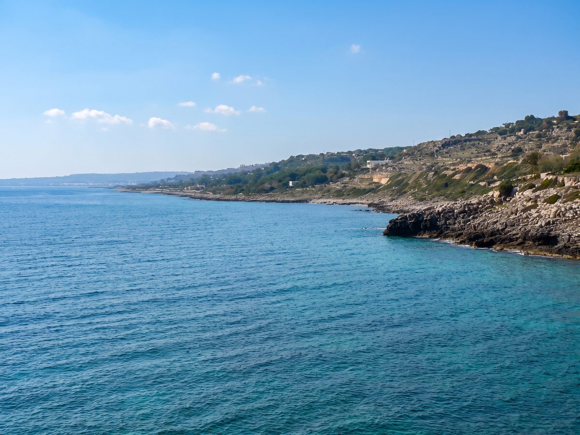 La costa di roccia e macchia di San Gregorio che si allunga sul mare calmo, vista dalla baia