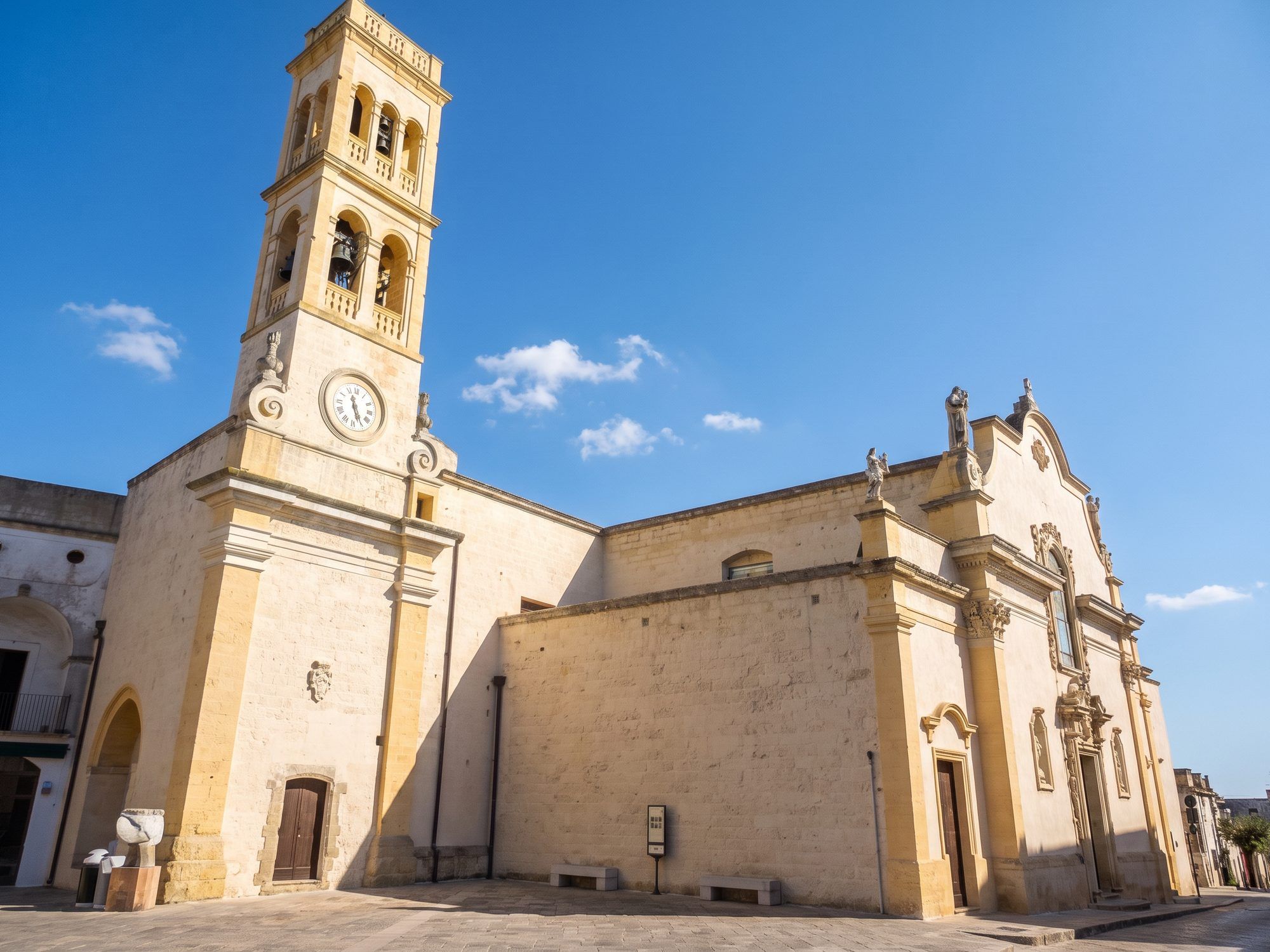 La chiesa madre di Specchia con il campanile e l'orologio, in pietra gialla, sotto il cielo azzurro