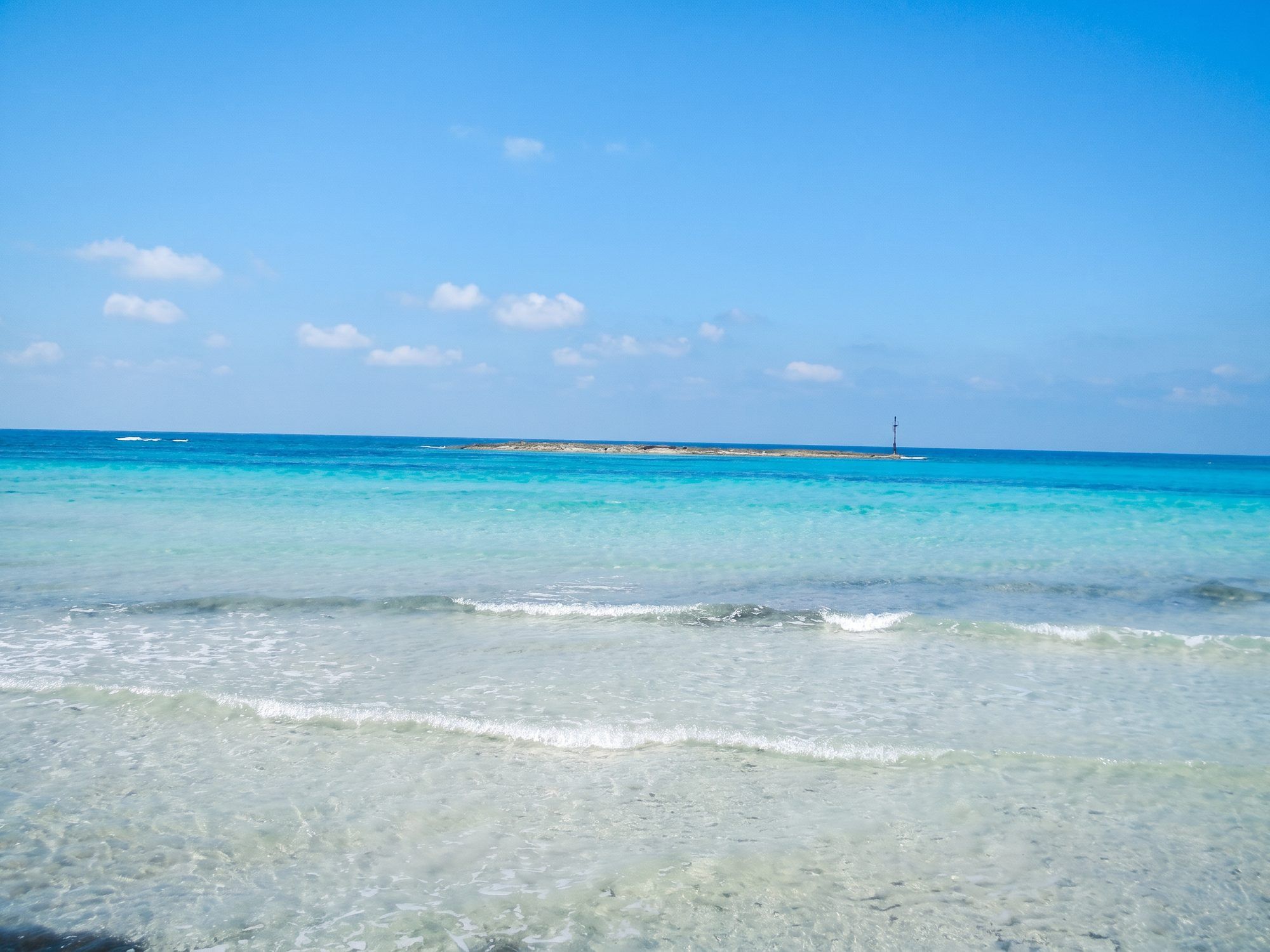 Acqua bassa e trasparente sulla riva di Torre San Giovanni, con un isolotto basso all'orizzonte