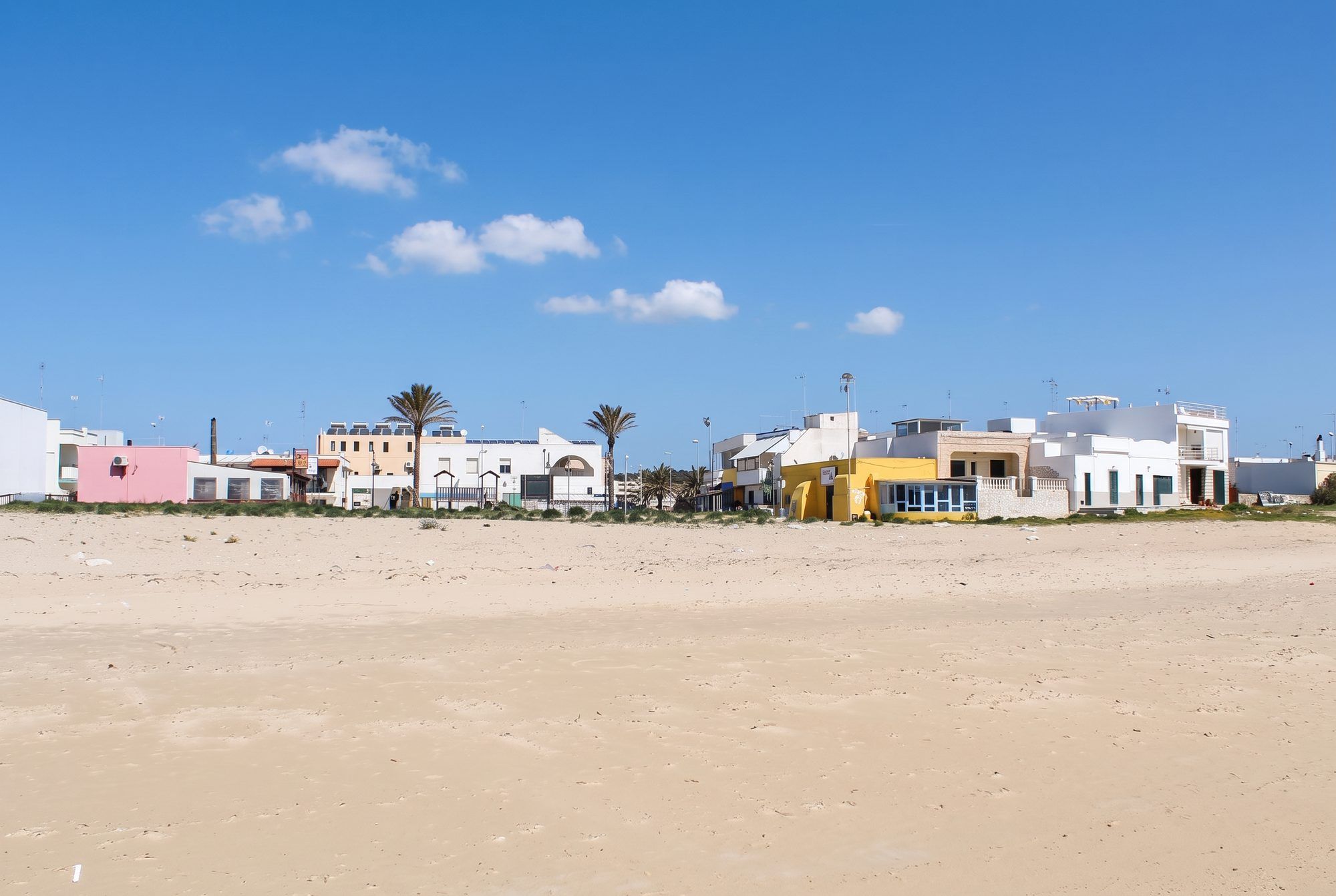 Le case bianche, gialle e rosa di Torre Pali con le palme, viste dalla spiaggia di sabbia