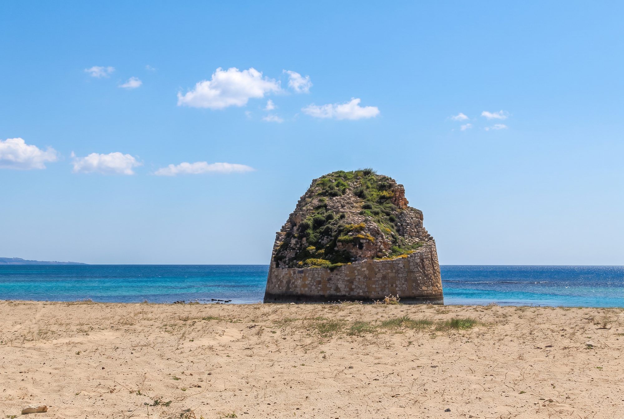 La torre di Torre Pali in mezzo al mare, vista dalla spiaggia con il mare blu e il cielo sereno