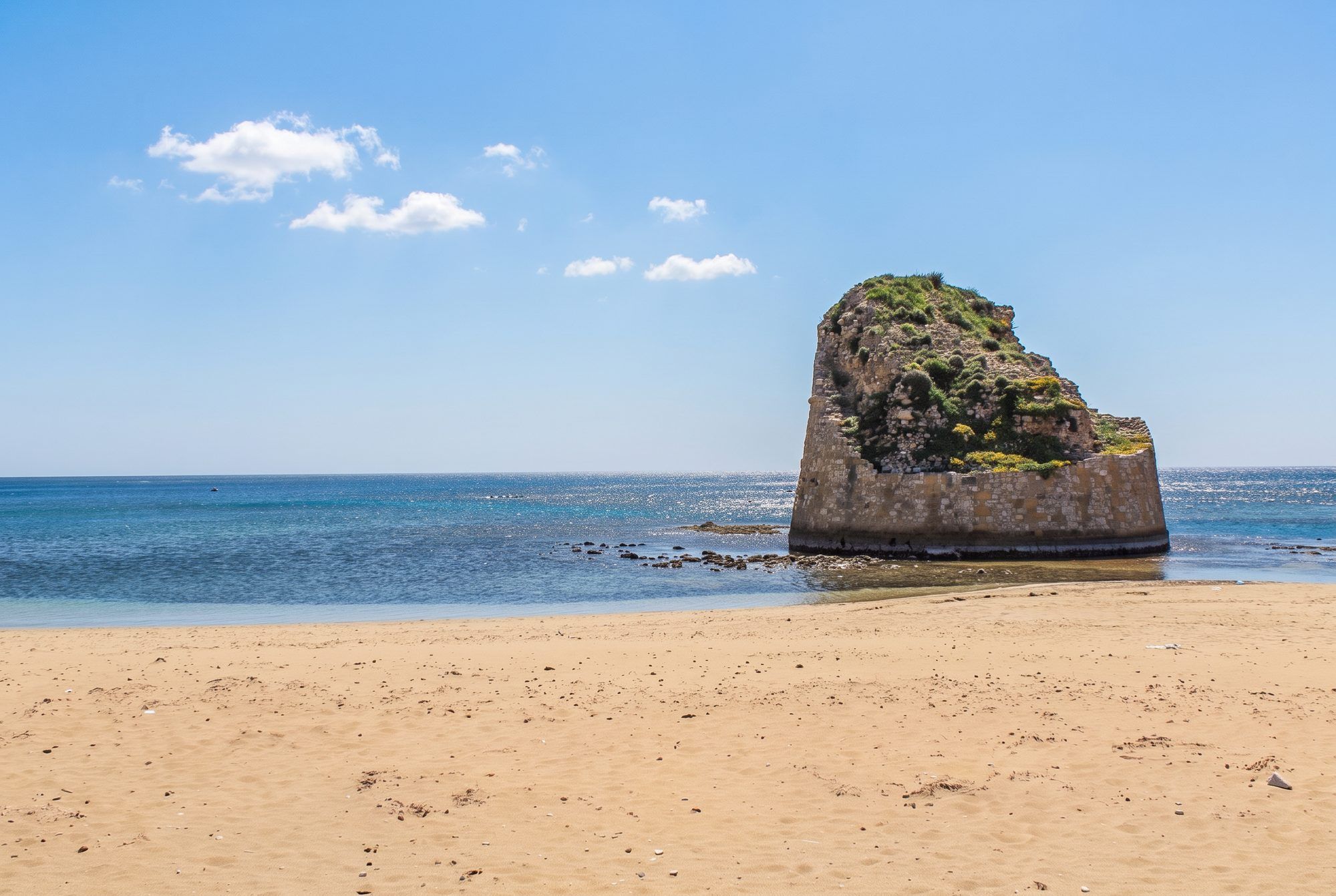 La torre di Torre Pali nel mare azzurro, davanti alla spiaggia di sabbia chiara