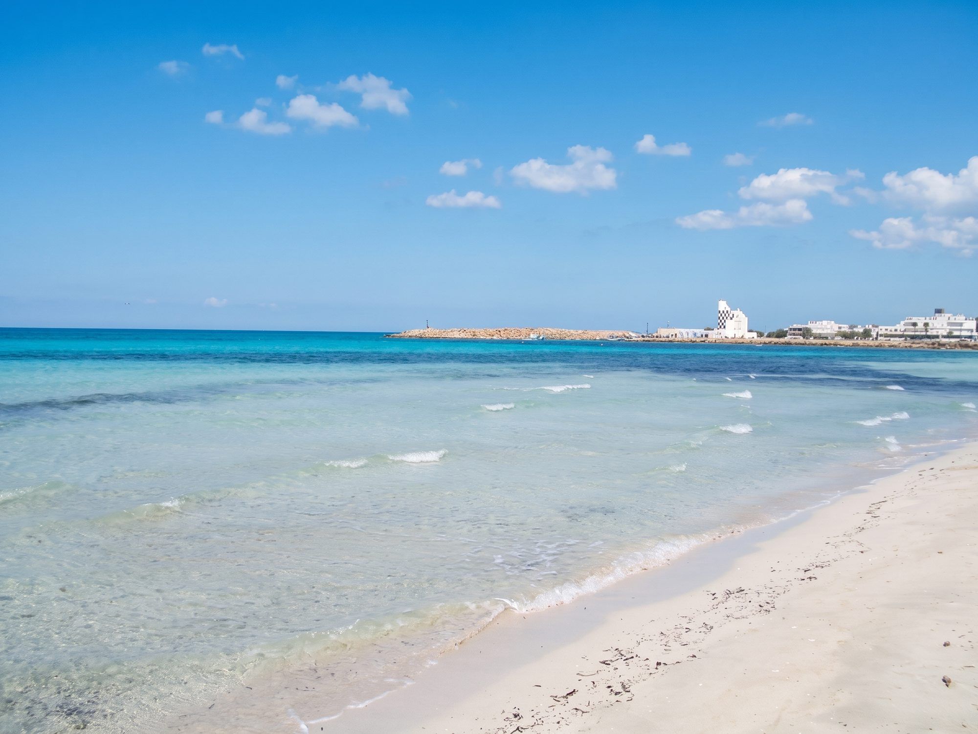 Sabbia chiara e acqua turchese a Torre San Giovanni, con il porto e le case bianche in fondo